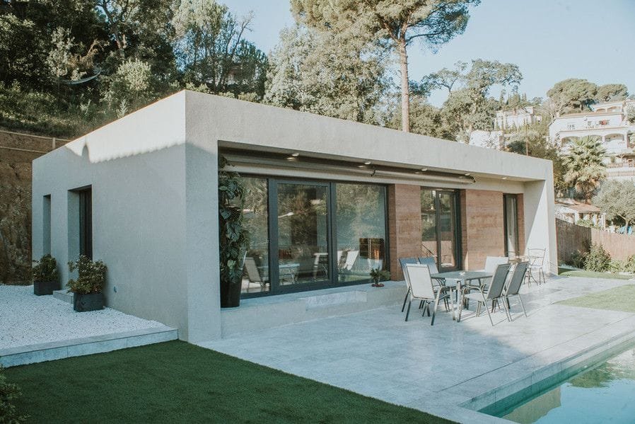 Foto de una casa del Modelo Especial de Cases Caliu: vivienda de una planta con fachada blanca, grandes puertas correderas y terraza junto a la piscina